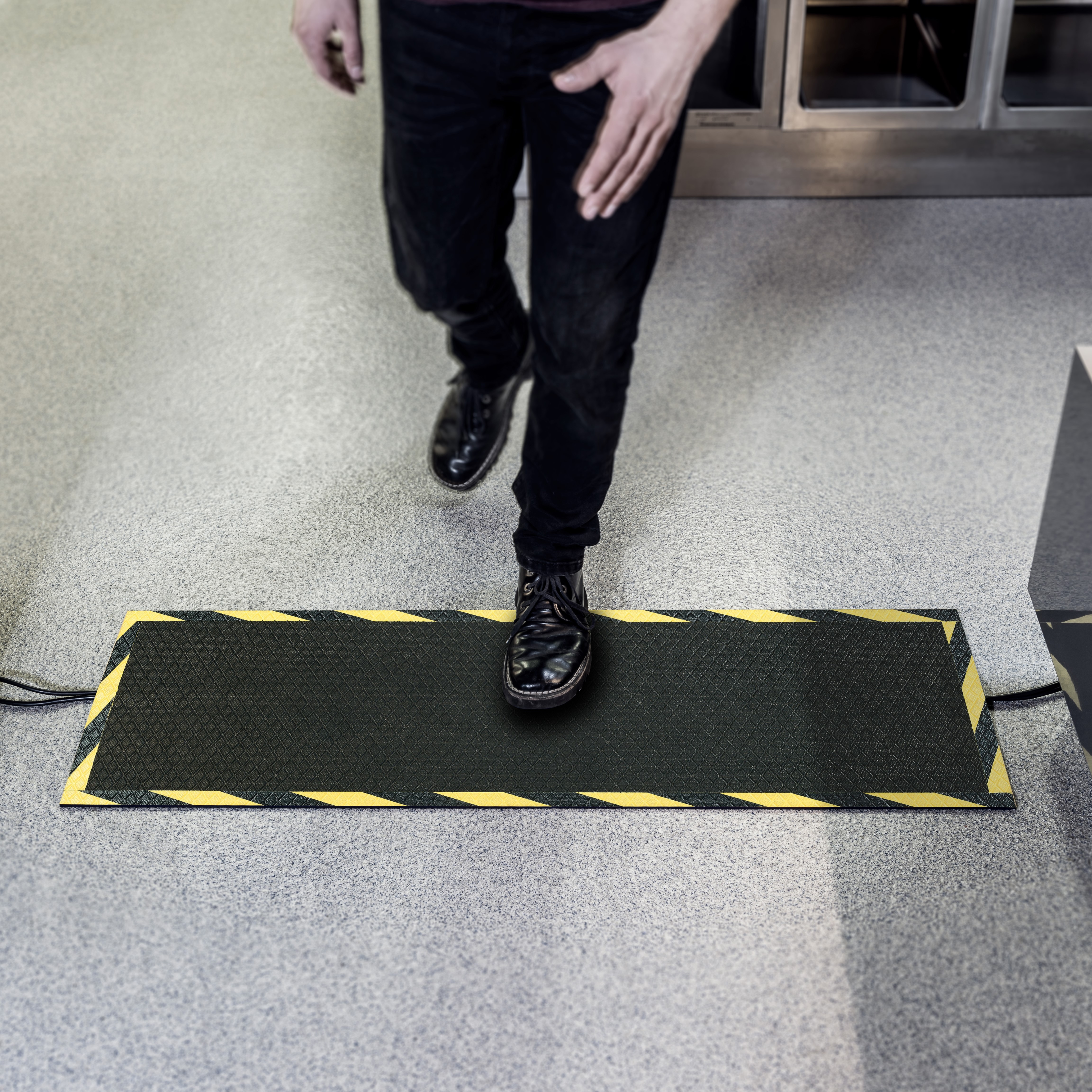 schwarze Kabelmatte im Büro zur Sicherung eines Kabels mit dem Unterkörper einer Person auf der Matte
